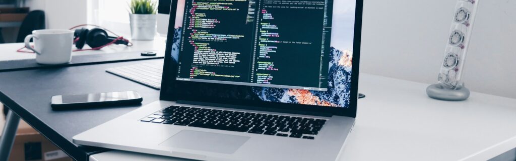 A MacBook with lines of code on its screen on a busy desk
