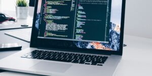 A MacBook with lines of code on its screen on a busy desk