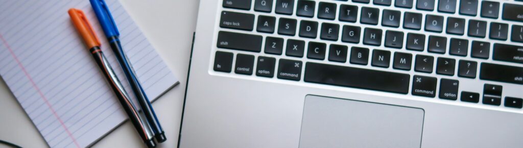 silver laptop computer beside white ruled paper